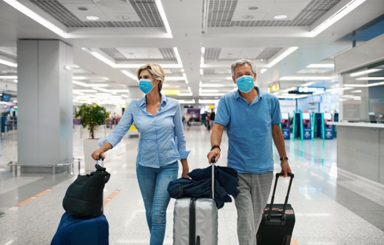 Closeup front view of a mid 50's couple waiting for a flight after coronavirus travel ban has been lifted. Both wearing face mask while walking through almost empty airport.