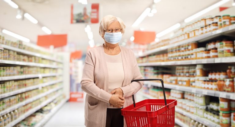 Senior female customer with a shopping basket in a supermarket wearing a protective medical mask