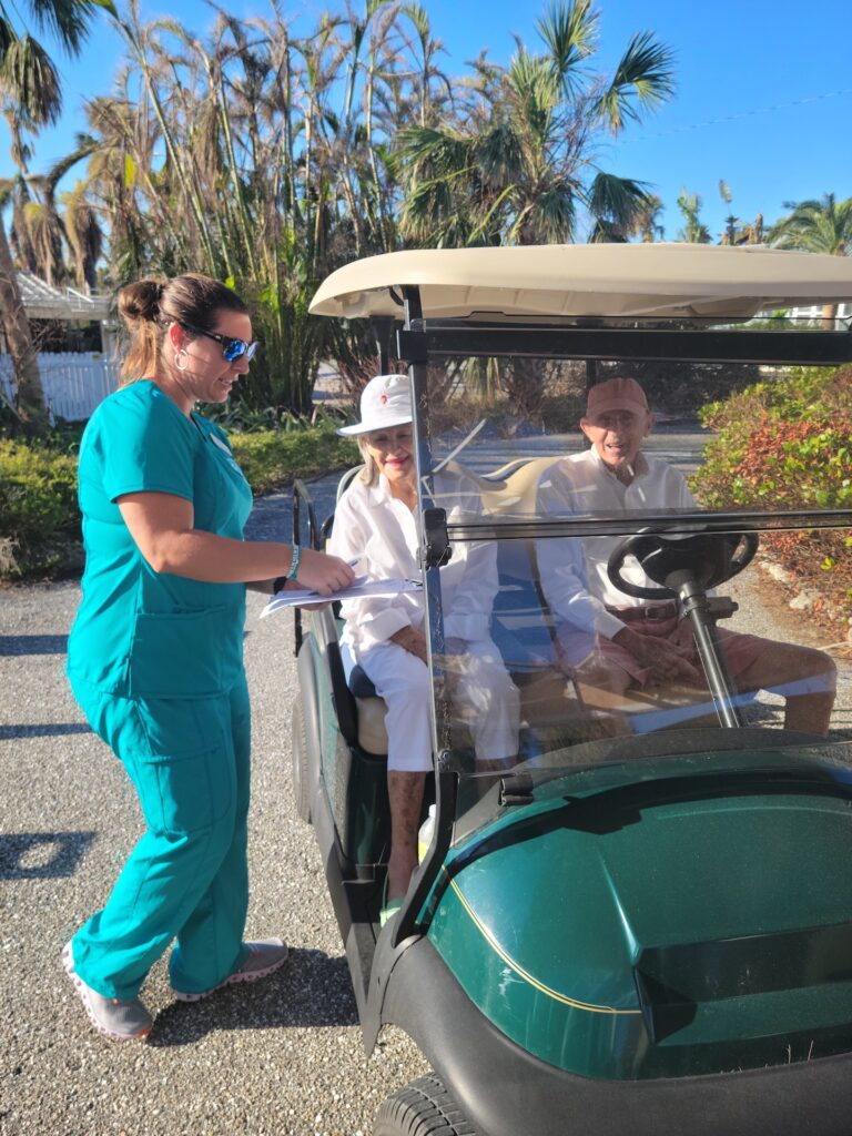 nurse standing with paperwork next to old couple in golf cart